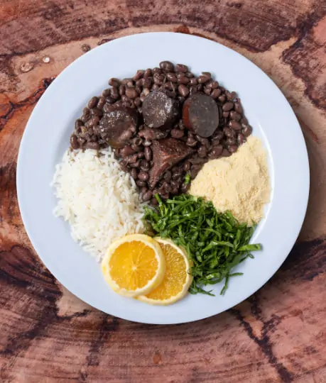 Prato branco com feijoada, arroz, laranja, couve e farofa.