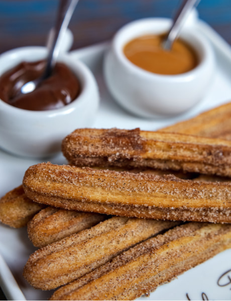 Churros acompanhado de dua s tigelas, uma de chocolate e outra de doce de leite.